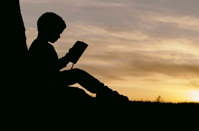 Imagem da silhueta de uma criança lendo a bíblia