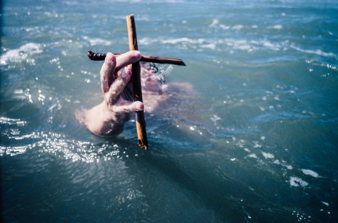 Imagem da mão de uma pessoa saindo da água e segurando uma cruz
