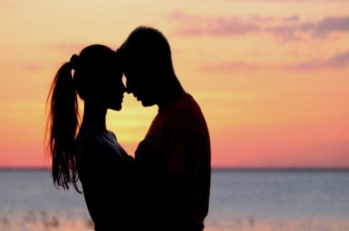 Imagem da silhueta de casal abraçados formando um coração no por do sol