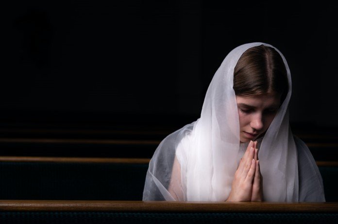 Imagem de moça com véu branco rezando de joelhos na igreja