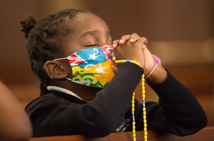 Imagem de criança de máscara orando com os olhos fechados