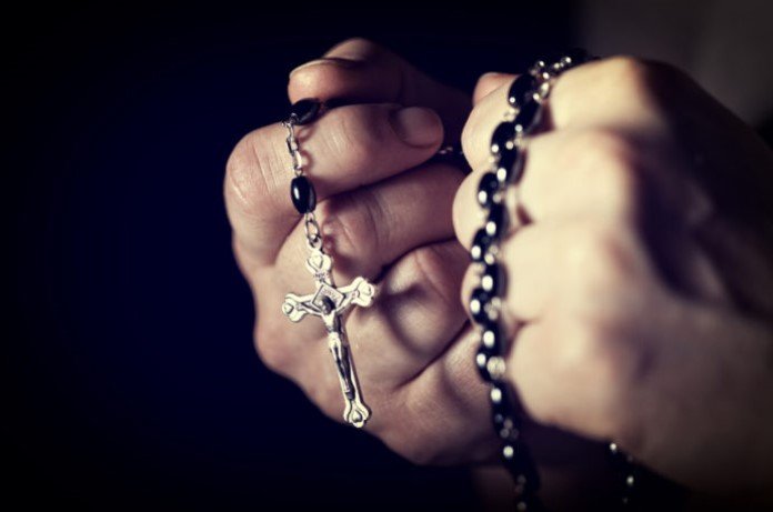 Imagem de duas mãos segurando um crucifixo com força